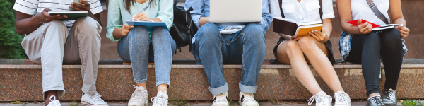Five students, seen from the waist down, sitting on stone steps, engaged in learning with digital devices and books.